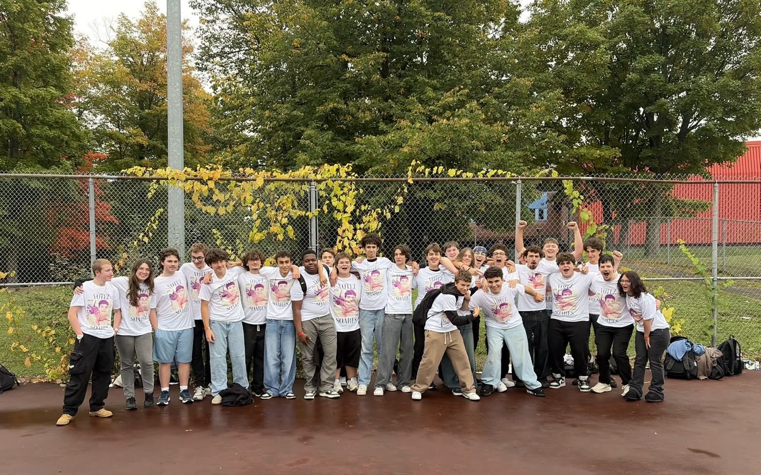 Une trentaine d'élèves réunis dehors, tous vêtus du t-shirt blanc « Votez Soares », posent ensemble en souriant et en levant le poing